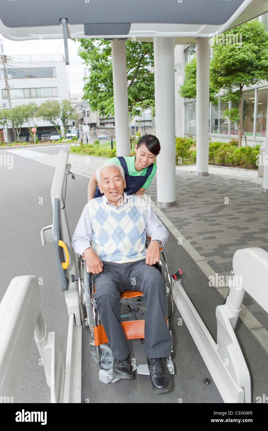 Healthcare worker helping senior man in wheelchair getting into a van, Kanagawa Prefecture, Honshu, Japan Stock Photo