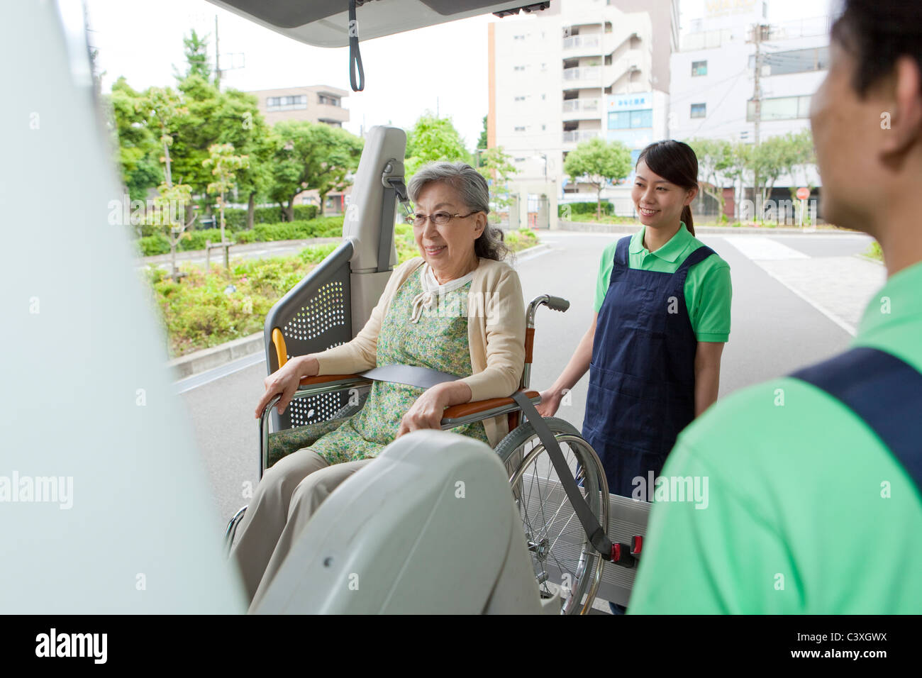 Healthcare workers helping senior woman in wheelchair getting into a van, Kanagawa Prefecture, Honshu, Japan Stock Photo