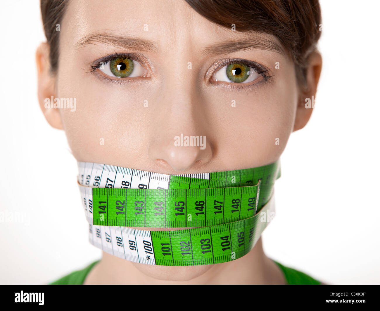 Portrait of a young woman with a green measuring tape covering the mouth Stock Photo