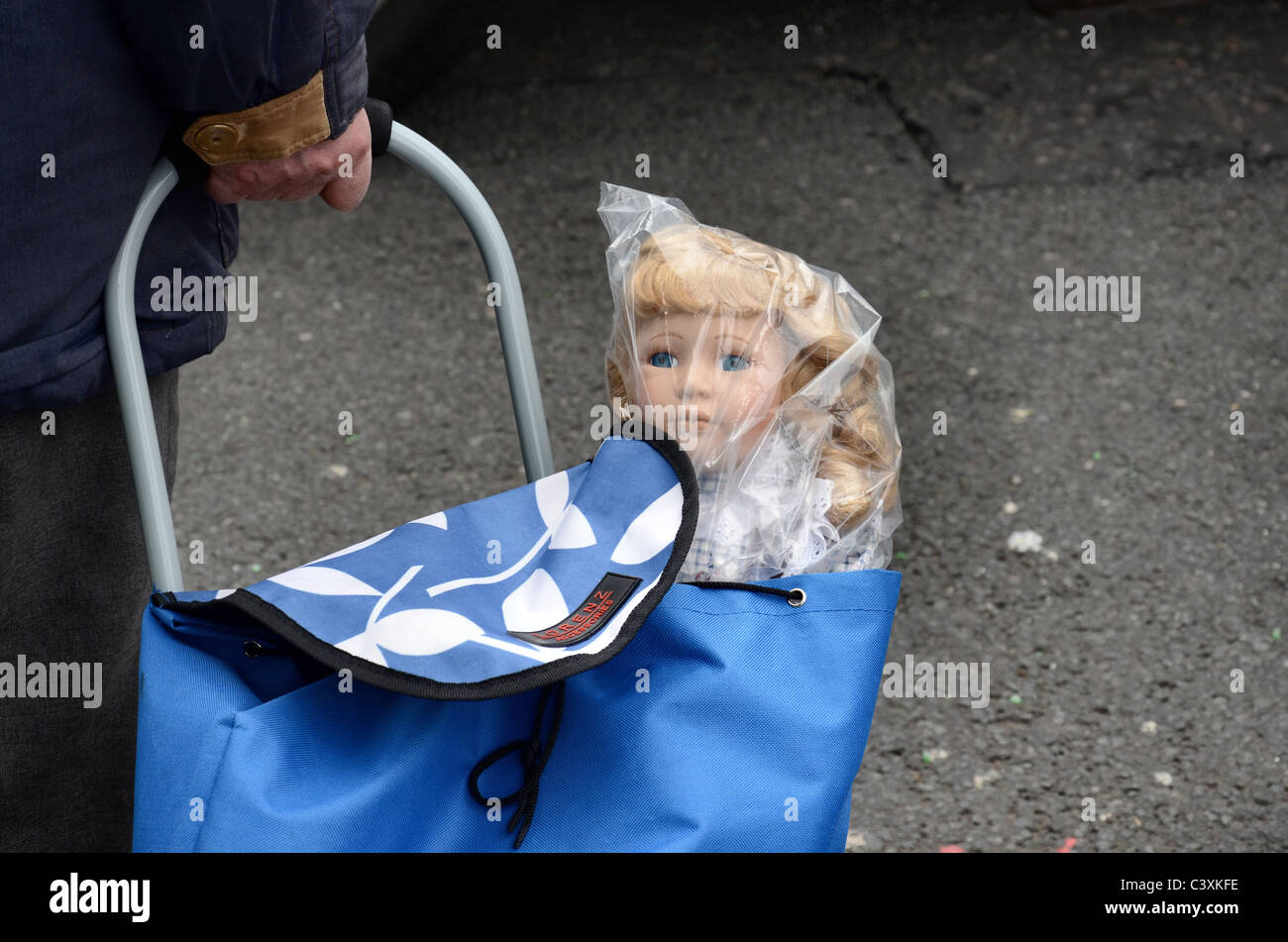 A child's doll in a plastic bag sticking out of a shopping trolley. Stock Photo