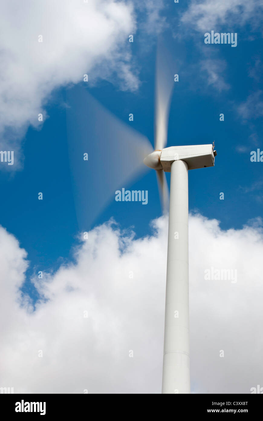 Wind turbine showing the blades moving against blue sky with clouds. Stock Photo