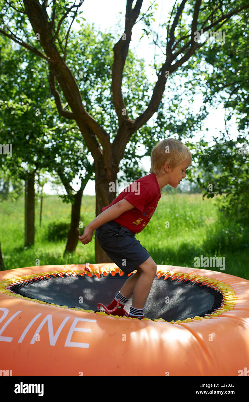 Happy Blond Child Boy Jumping and playing on orange Trampoline in Yard