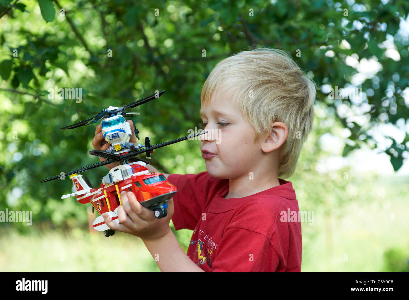 A Child Young Blond Boy Playing with a Toy Lego Firefighter Rescue Helicopter and Police Helicopter outdoors Stock Photo