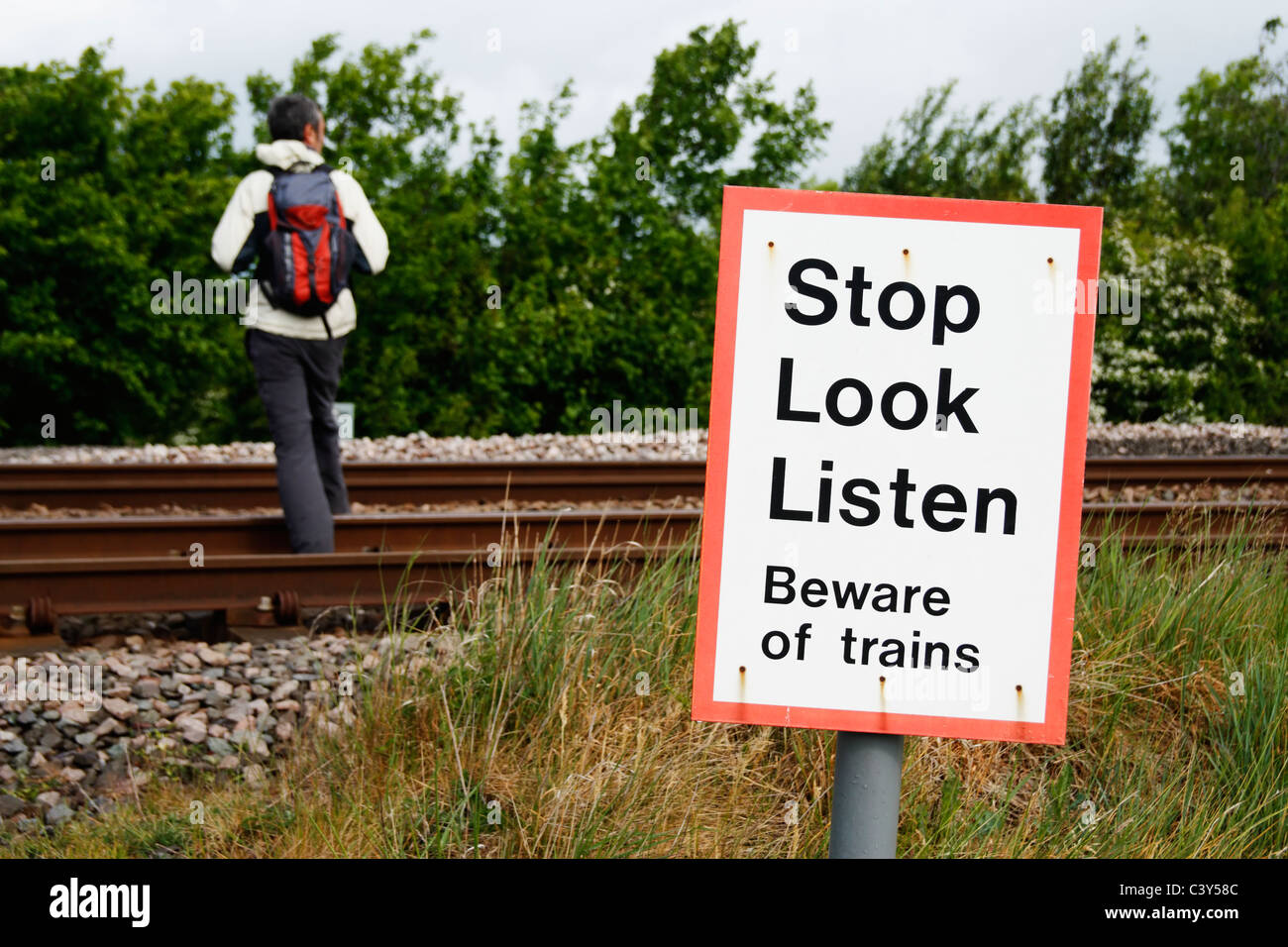 Hiker crossing railway line near beware of trains sign. UK Stock Photo