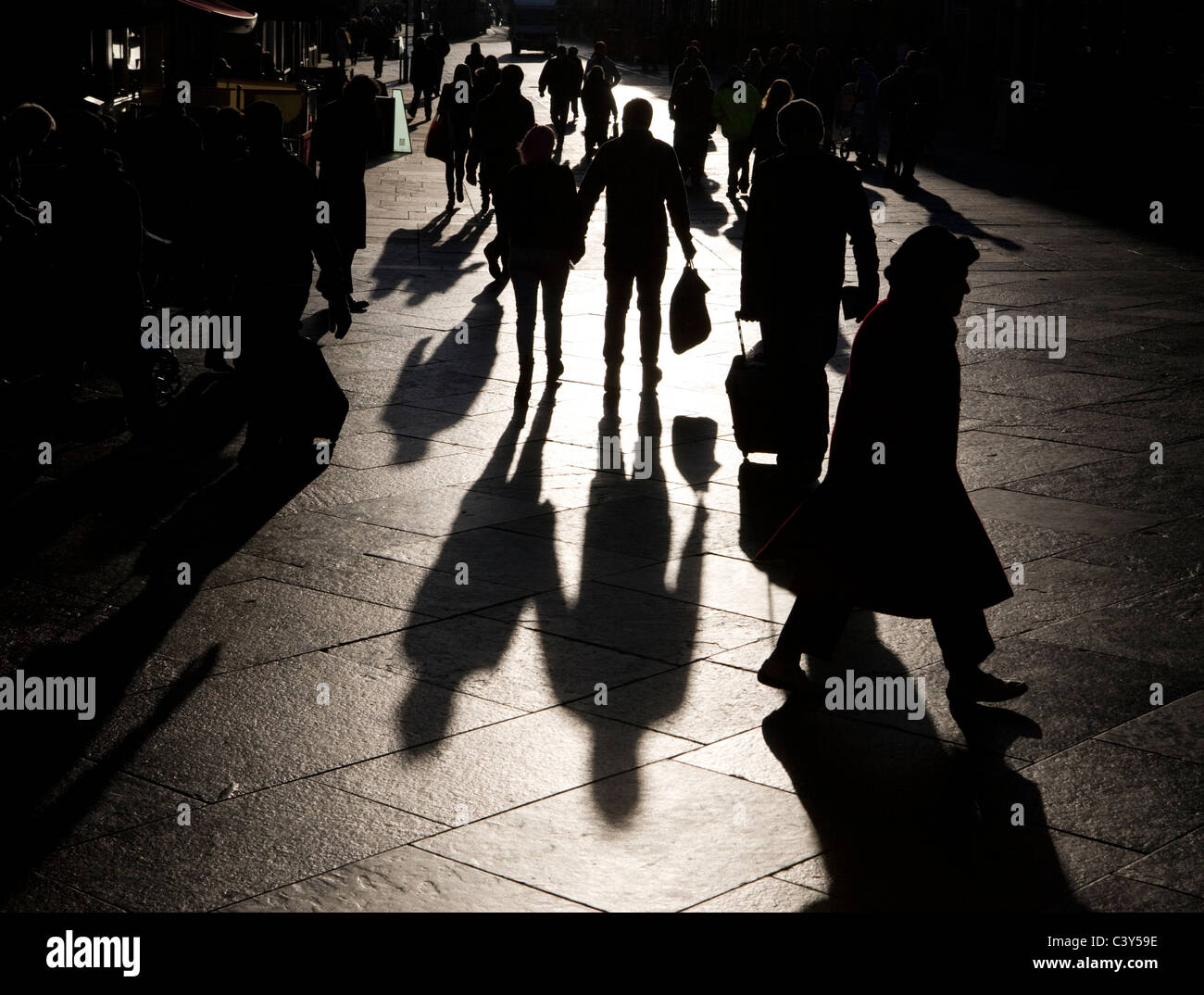 People shopping on a paved city street casting long shadows Stock Photo