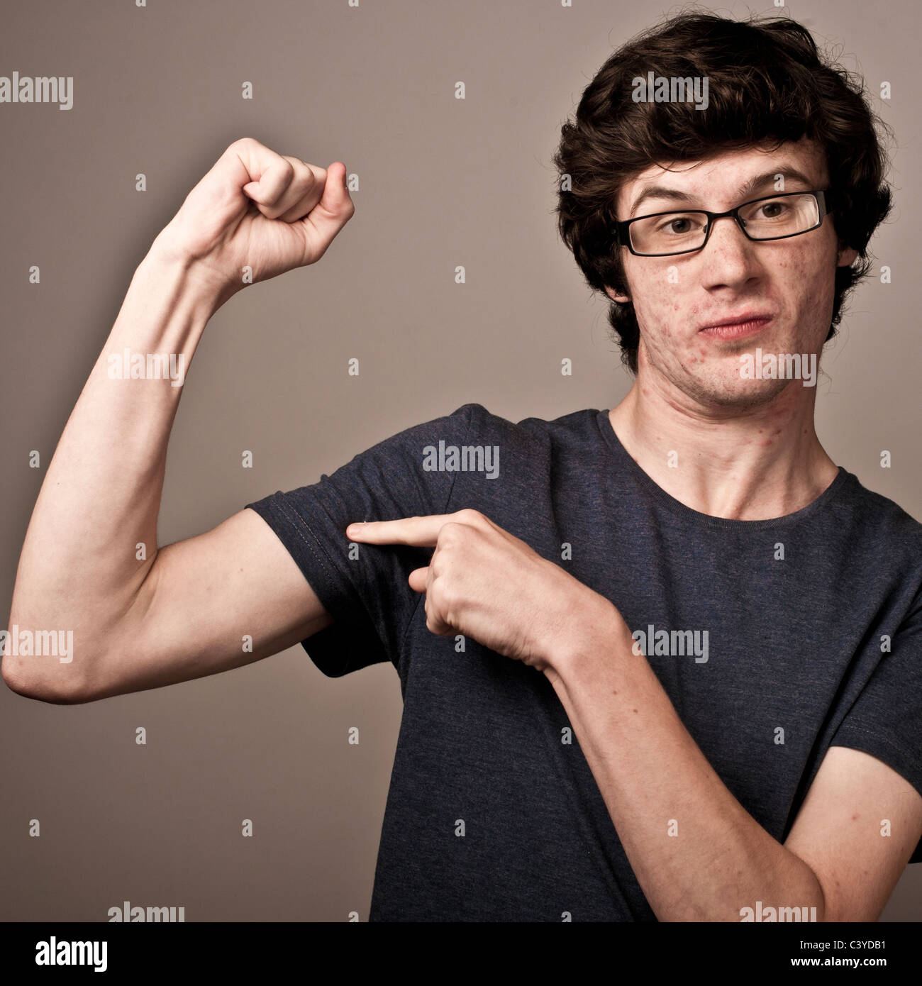 a weak feeble geek nerd young man with thin arms wearing glasses flexing his muscles Stock Photo