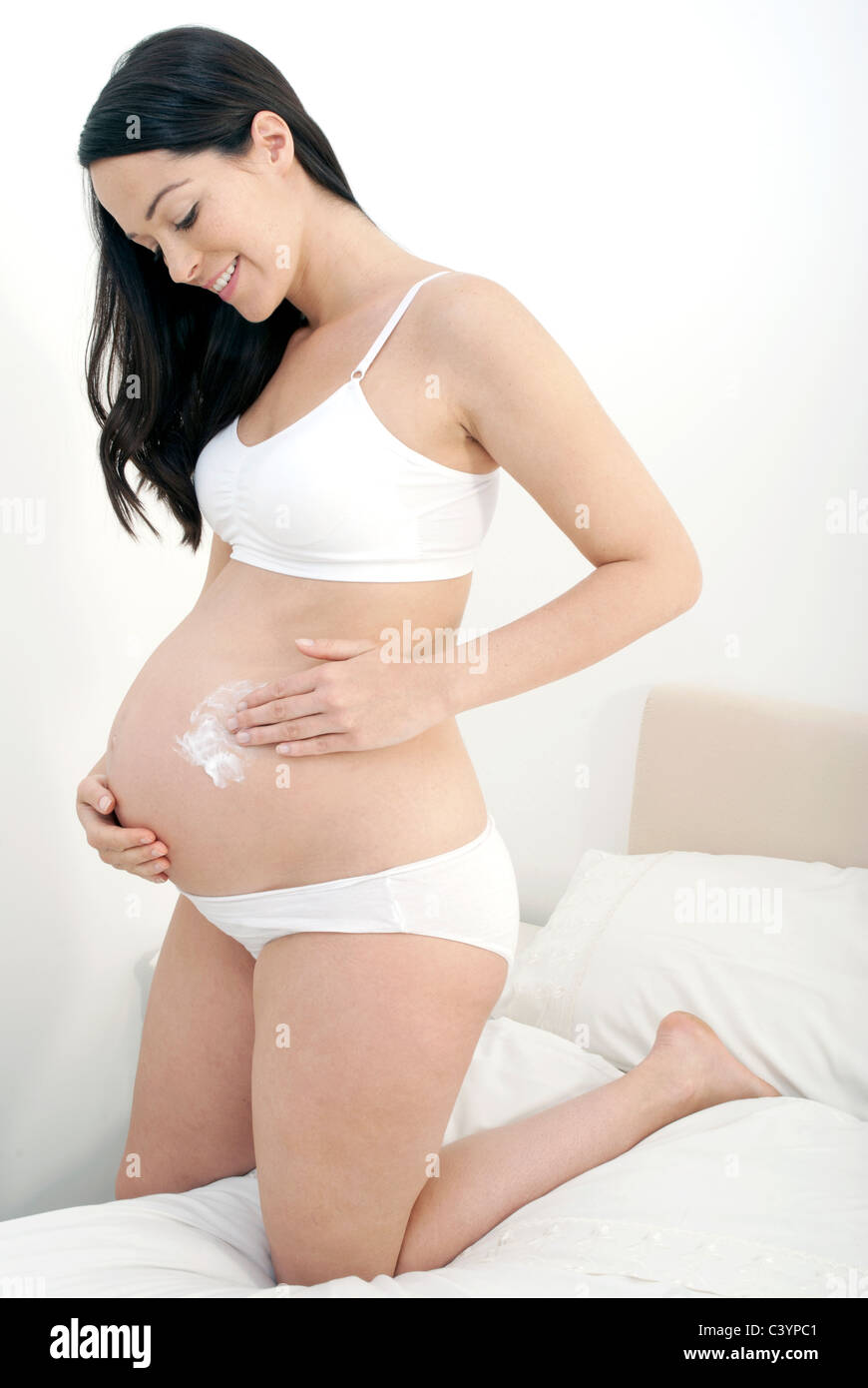 Pregnant woman apply cream to her growing bump Stock Photo