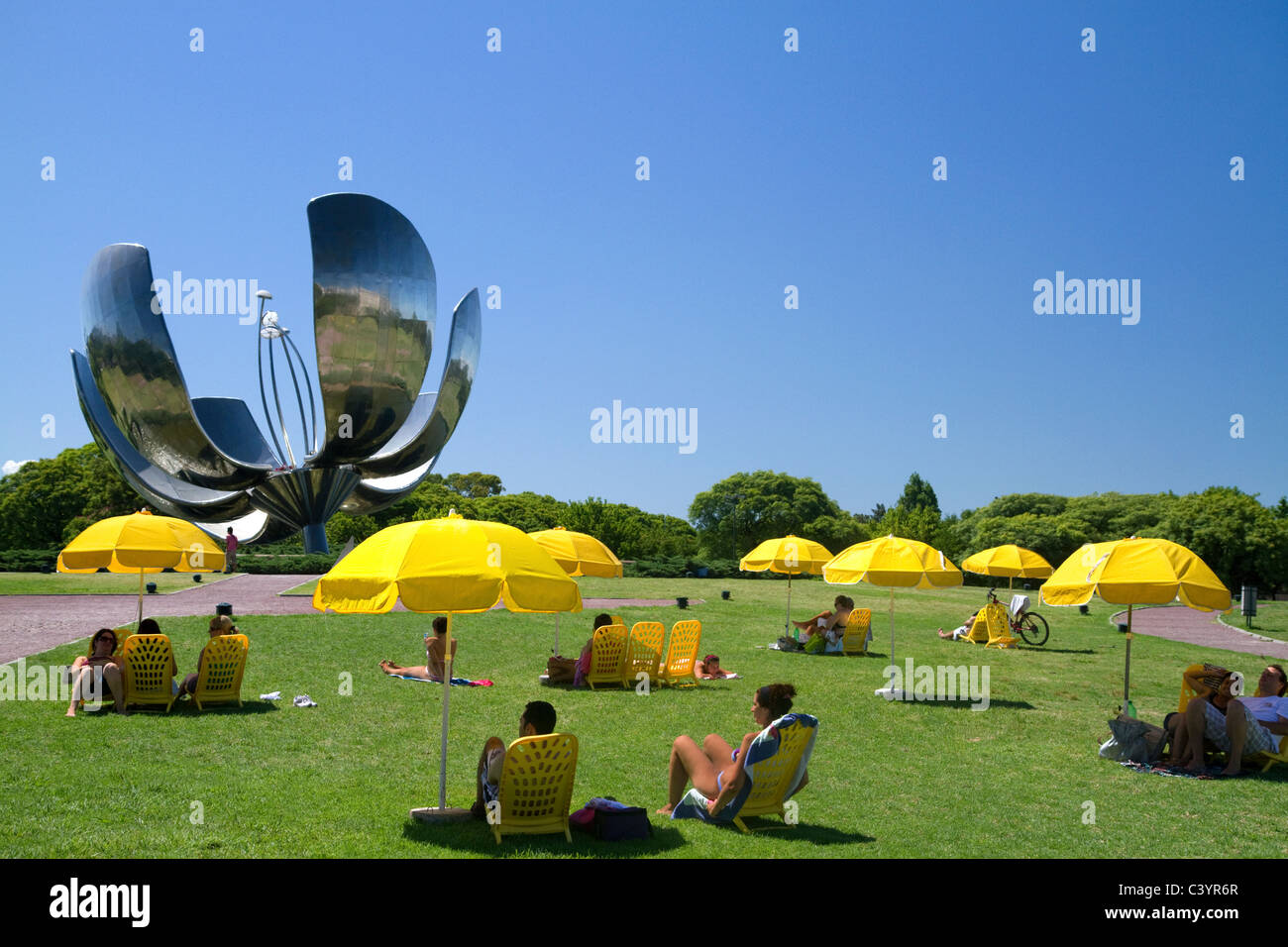 People sit under yellow umbrellas near the Floralis Generica sculpture at Plaza de las Naciones Unidas, Buenos Aires, Argentina. Stock Photo