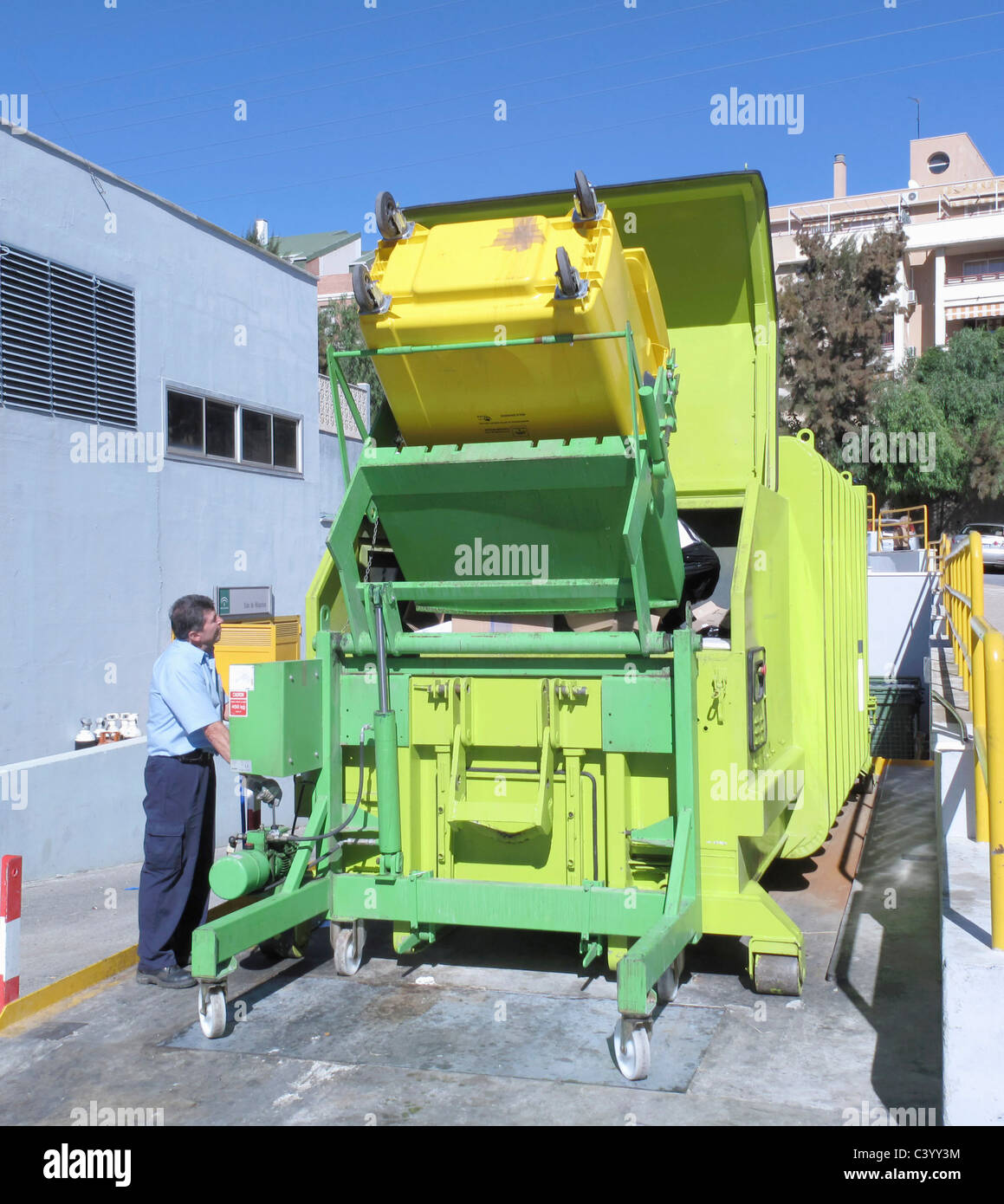 Operator tipping waste from trash bin into rubbish compactor at Clinica