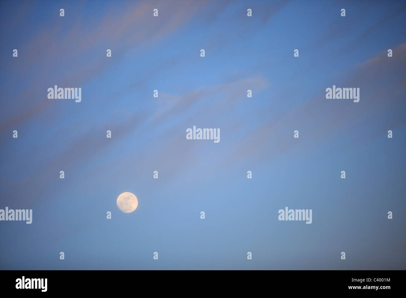 Full moon rises under a twilight sky and clouds Stock Photo