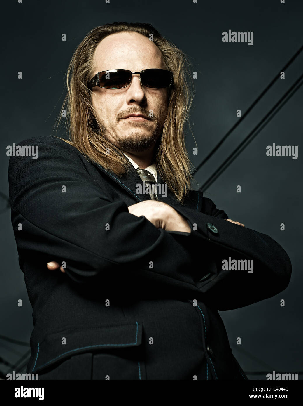 Low perspective shot of a long-haired, balding man standing with his arms crossed. Stock Photo