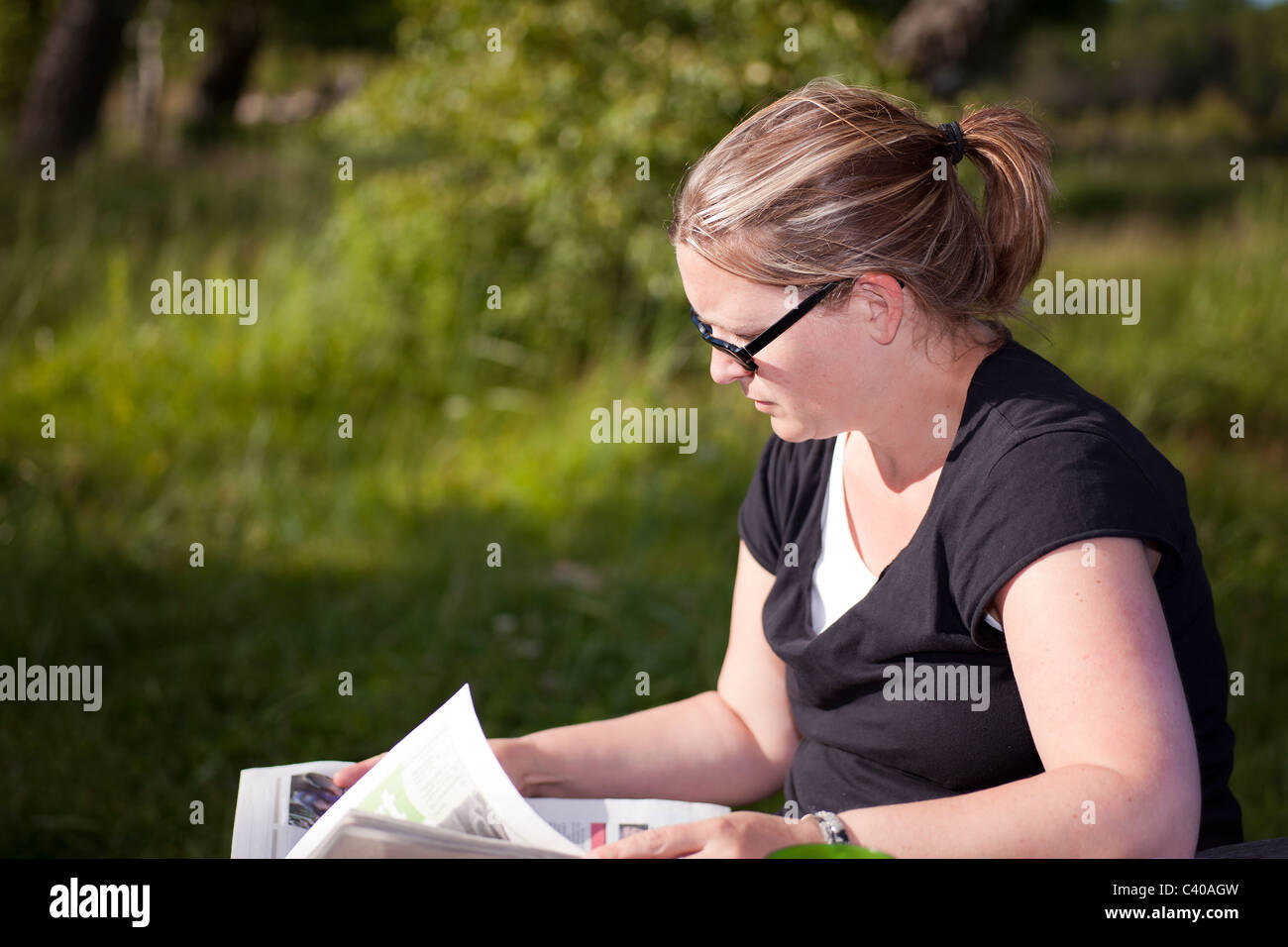 Woman sitting outdoors reading a newspaper Stock Photo - Alamy