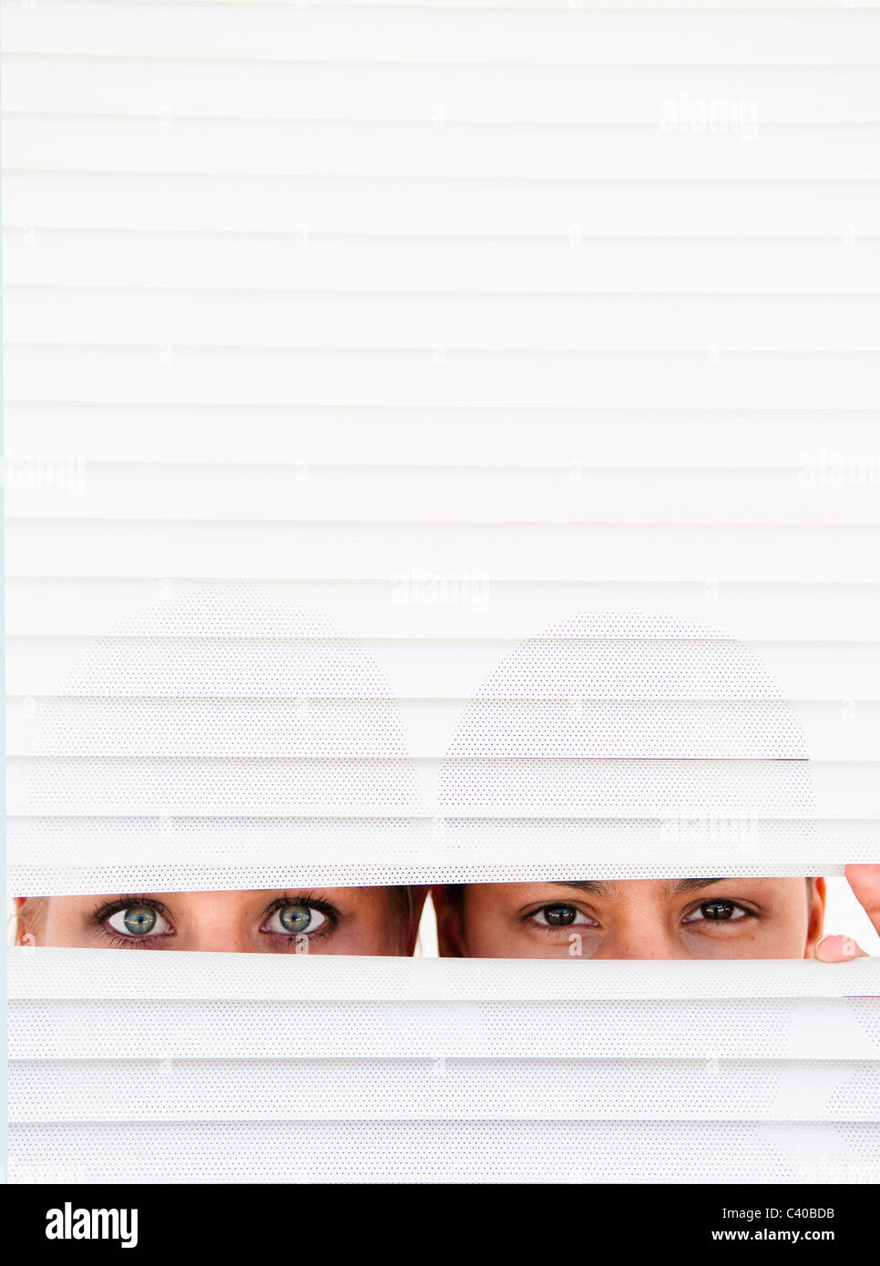 Two women look through blinds Stock Photo
