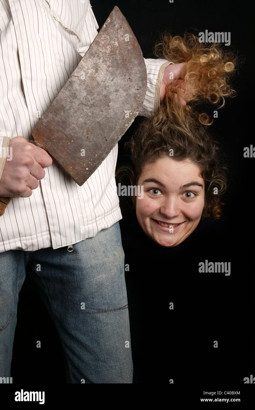 Humorous serial killer with big knife and severed head of smiling young woman Stock Photo