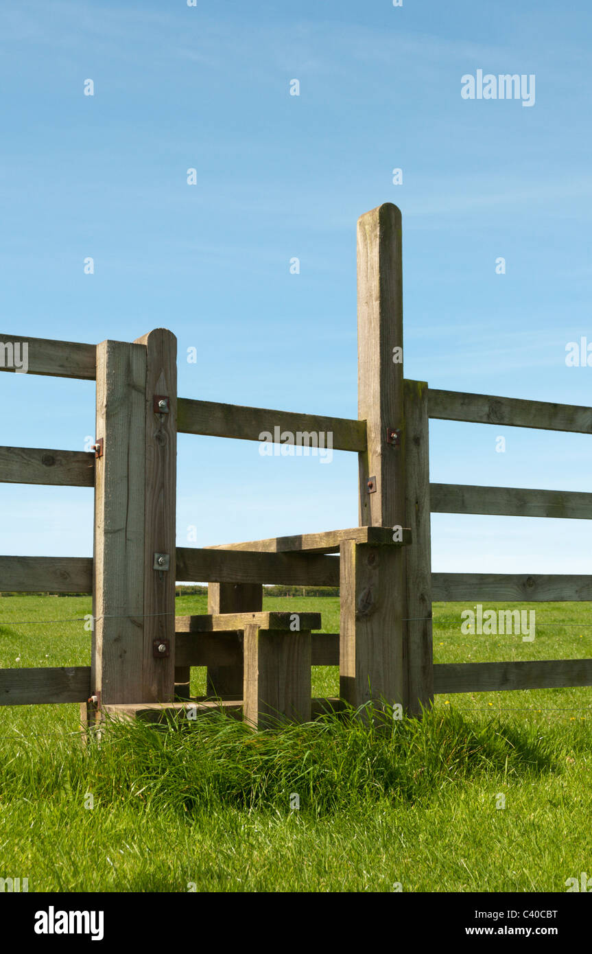 A wooden stile in a farm fence seen against a clear blue sky. Stock Photo