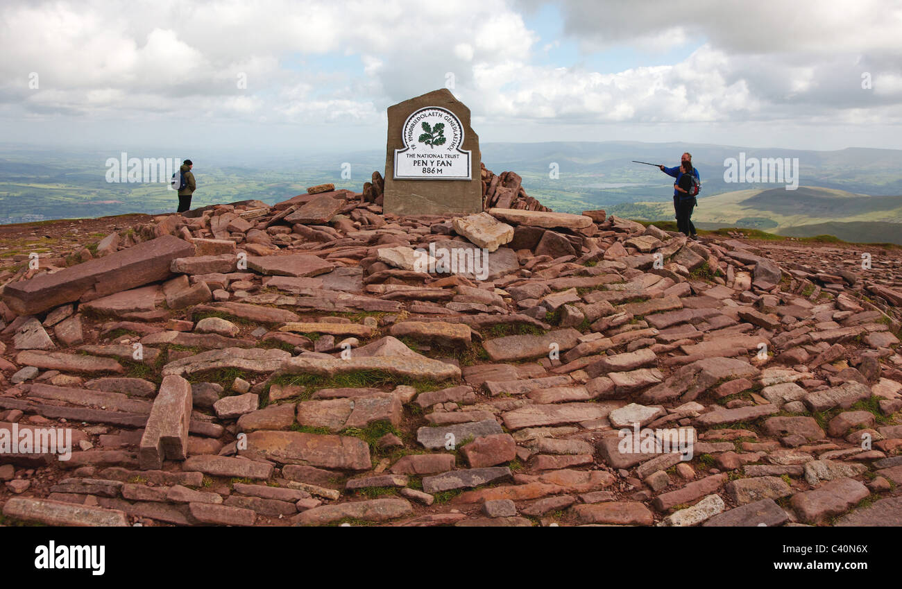 Walkers reaching the plaque crowning the old red sandstone summit cairn on Pen y Fan in the Brecon Beacons National Park South Wales Stock Photo