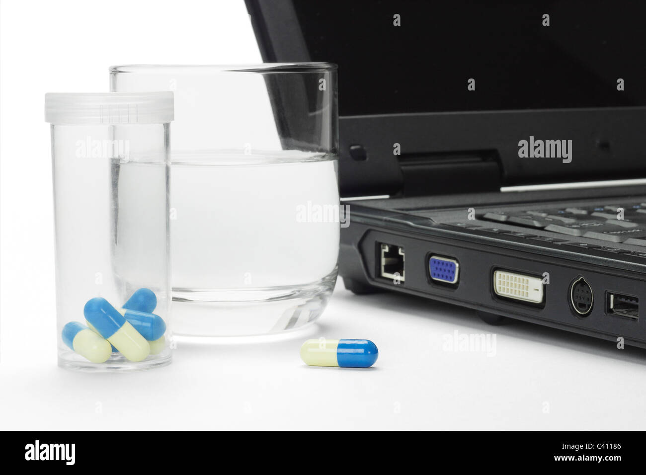 Pills and glass of water next to laptop - conceptual image of IT work related stress Stock Photo