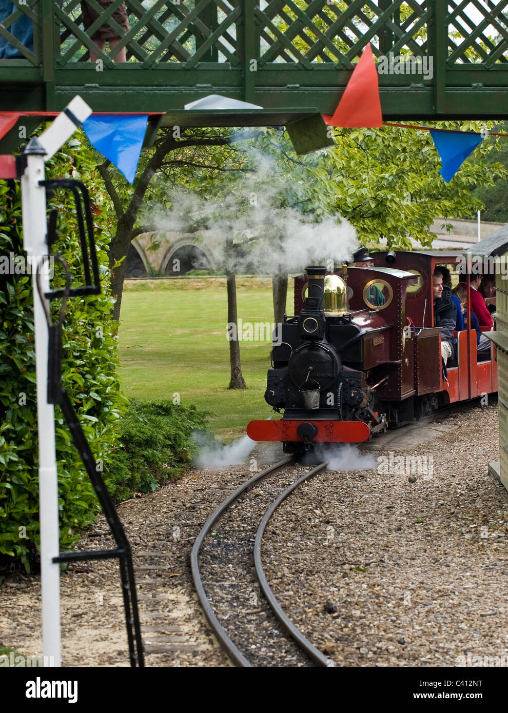 A miniature railway steam engine pulling carriages with passengers ...