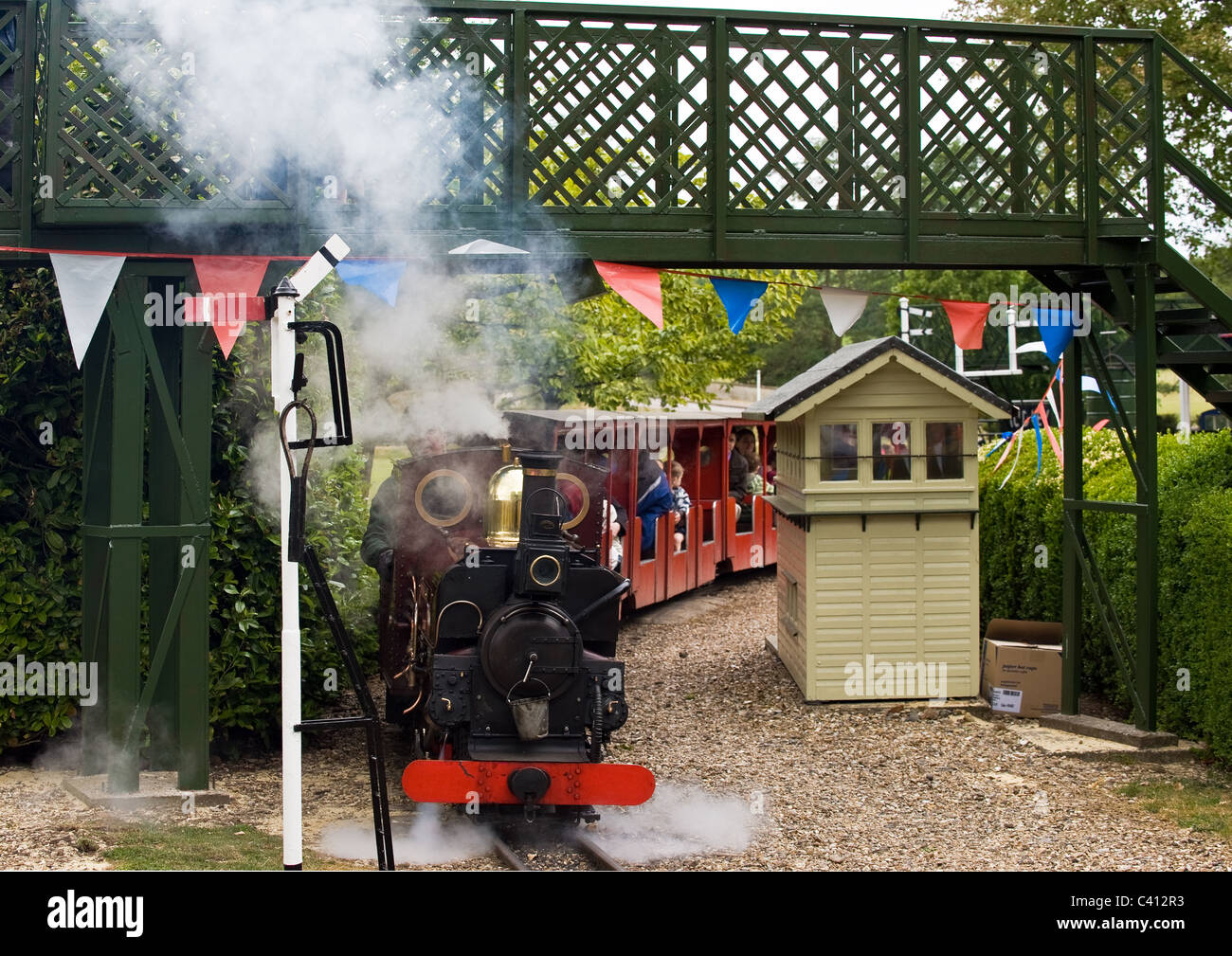 A miniature railway steam engine pulling carriages with passengers ...