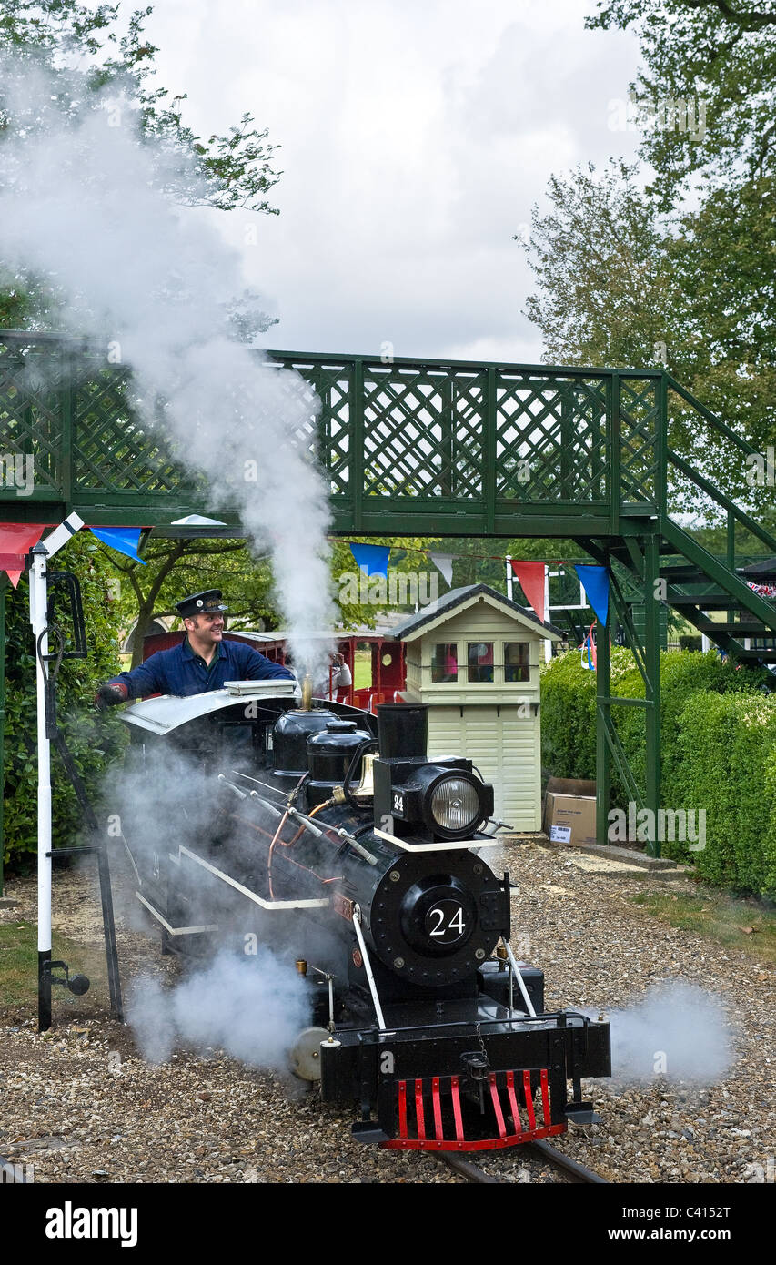 A miniature railway steam engine pulling carriages with passengers ...