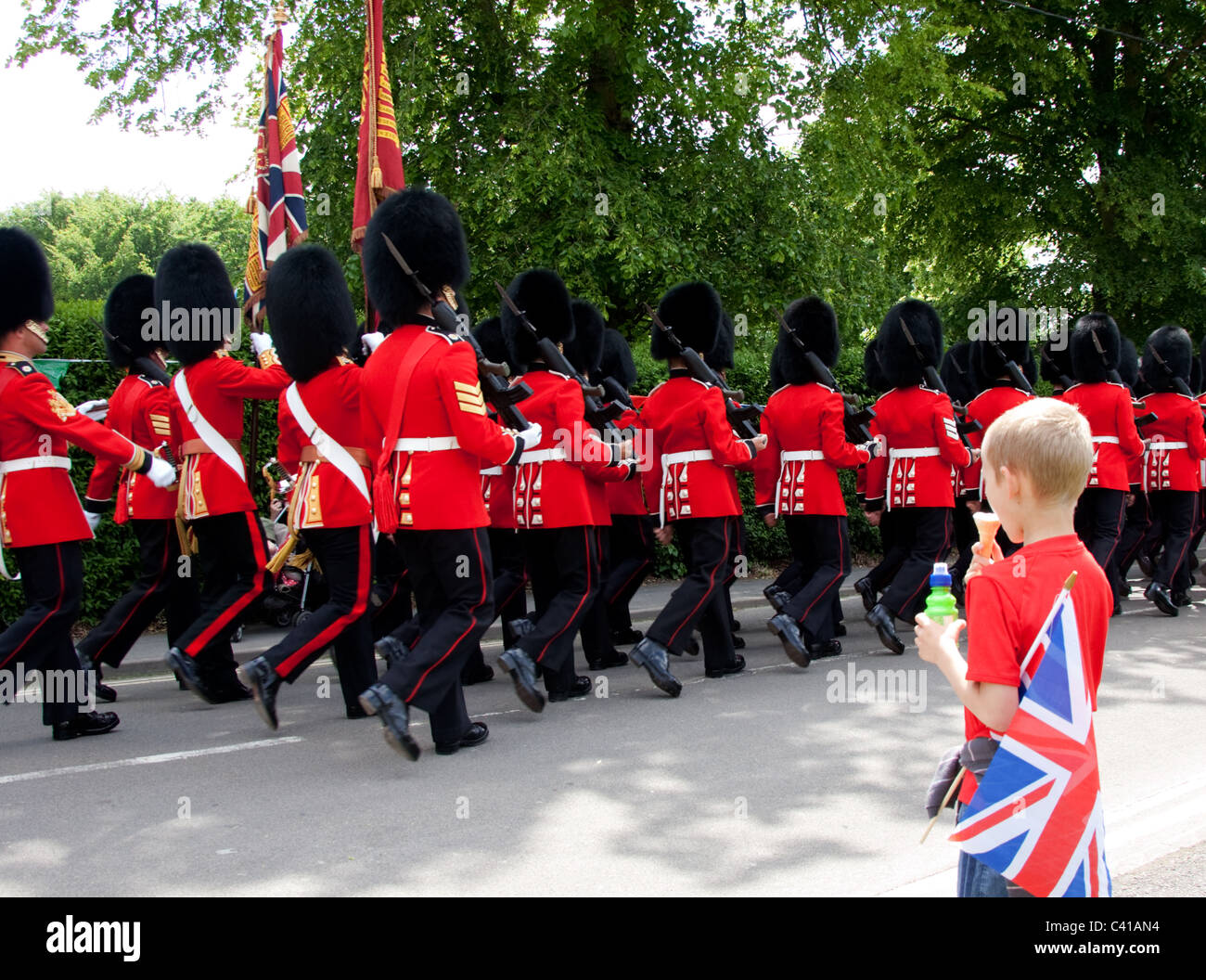 A young boy eating an ice cream cone and carrying a Union Flag watches a march-past of the Scots Guards on a sunny day. Stock Photo