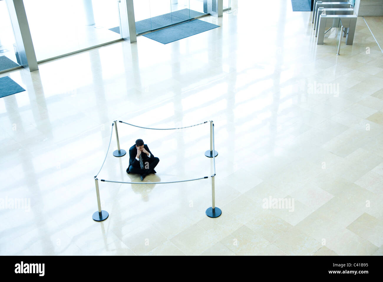 Businessman sitting on floor inside roped off area in lobby Stock Photo