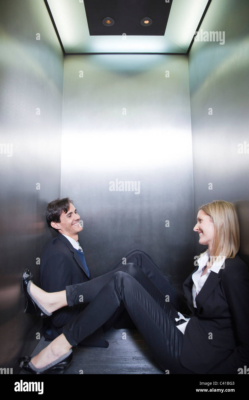 Professionals trapped in elevator, sitting on floor chatting Stock Photo