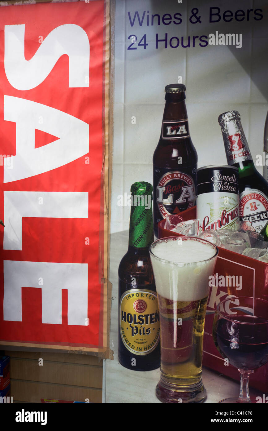 Sale sign and poster for alcoholic drinks like bottles of beer and glass of wine in a London off-license window. Stock Photo