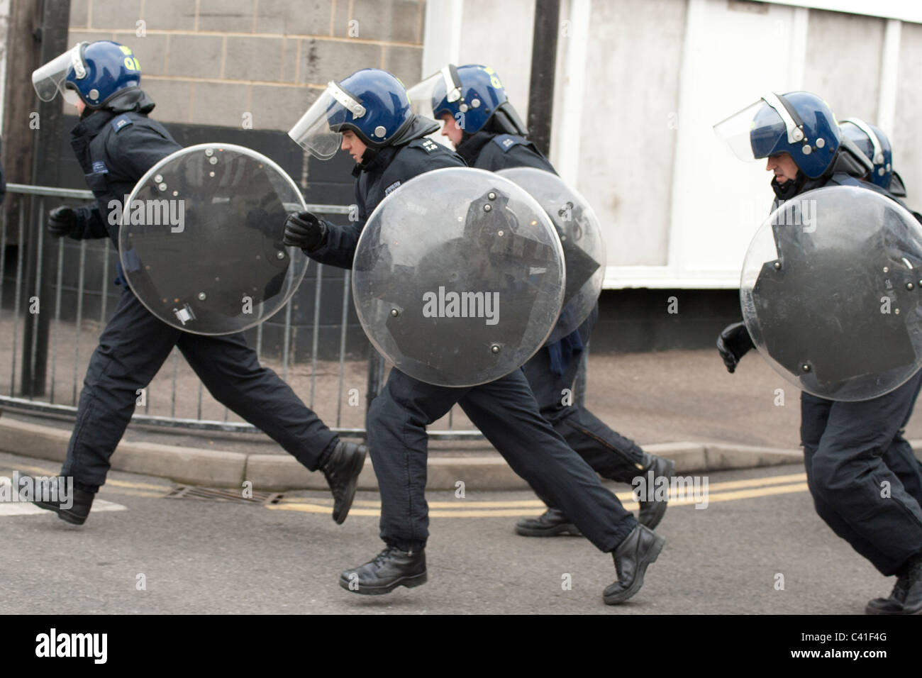 Police with short shields run round a corner during riot training. Stock Photo