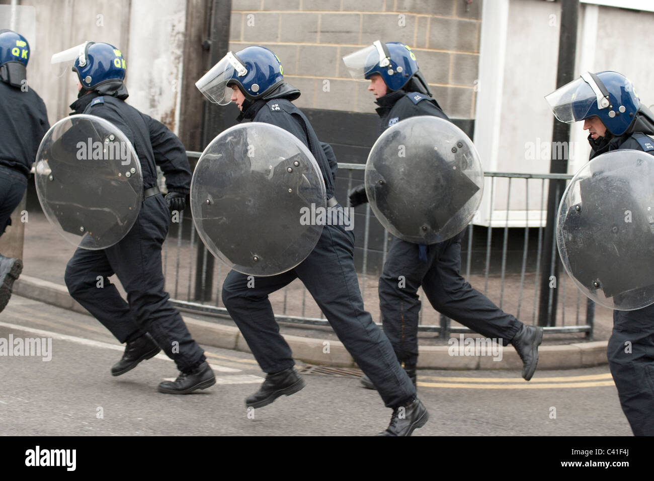 Police with short shields run round a corner during riot training. Stock Photo