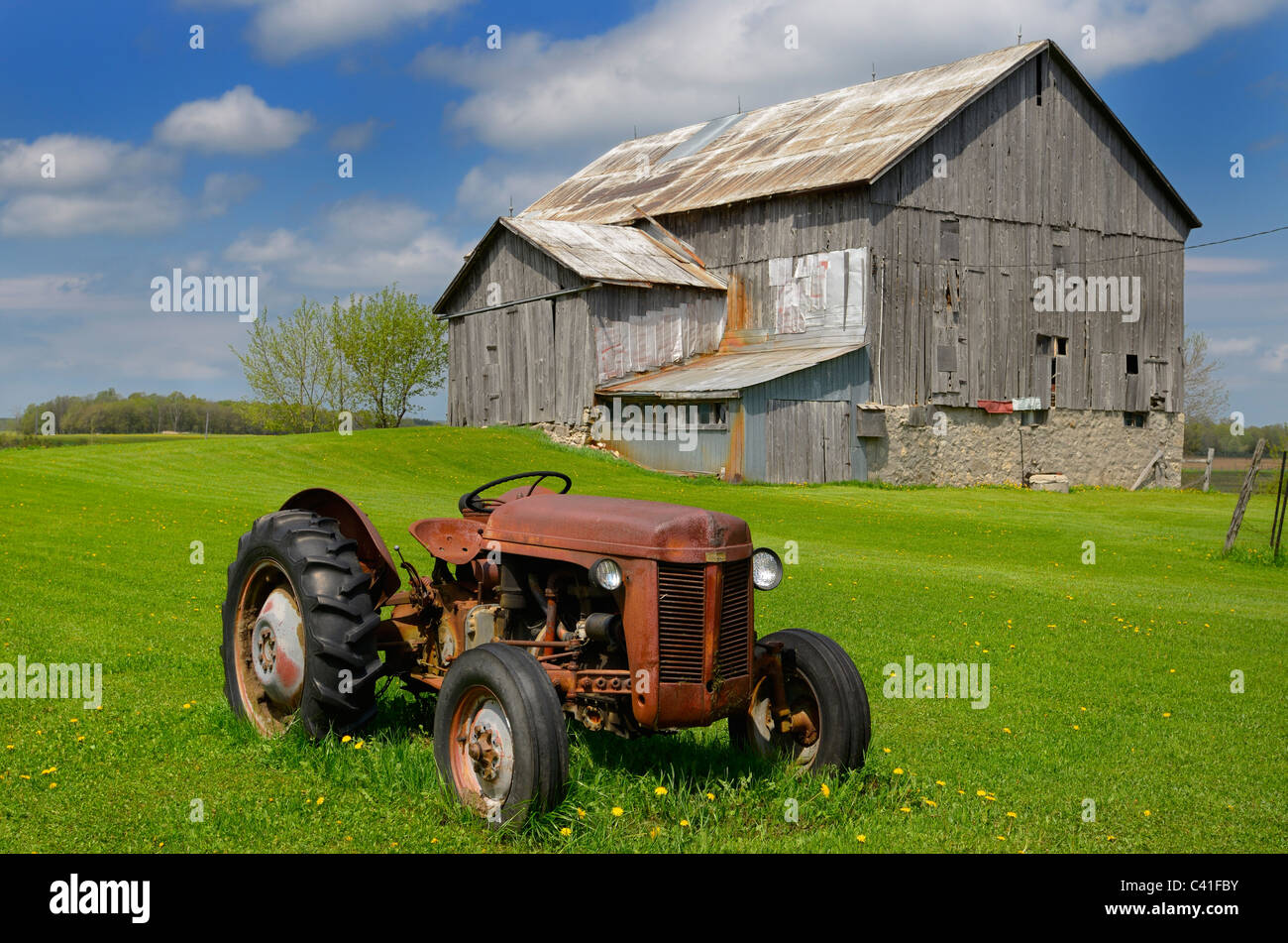 Rusted tractor and old barn in grass field and blue sky in rural Ontario Canada Stock Photo