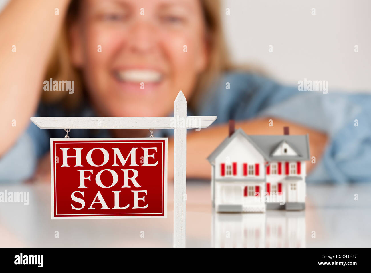 Happy Woman Behind Home For Sale Real Estate Sign and Model House on a ...