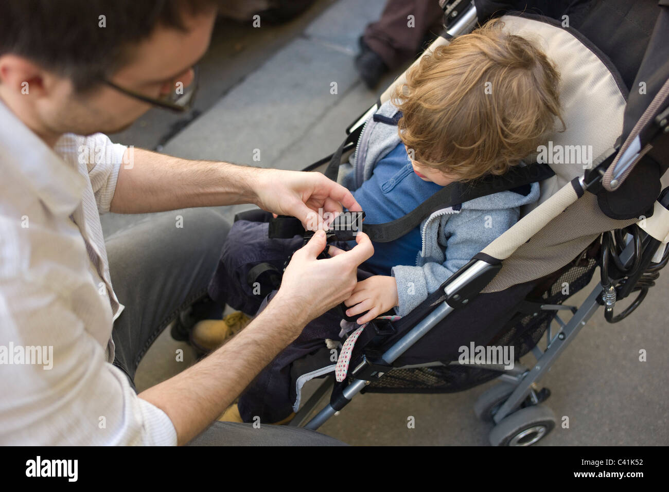 Father strapping toddler boy into stroller Stock Photo Alamy