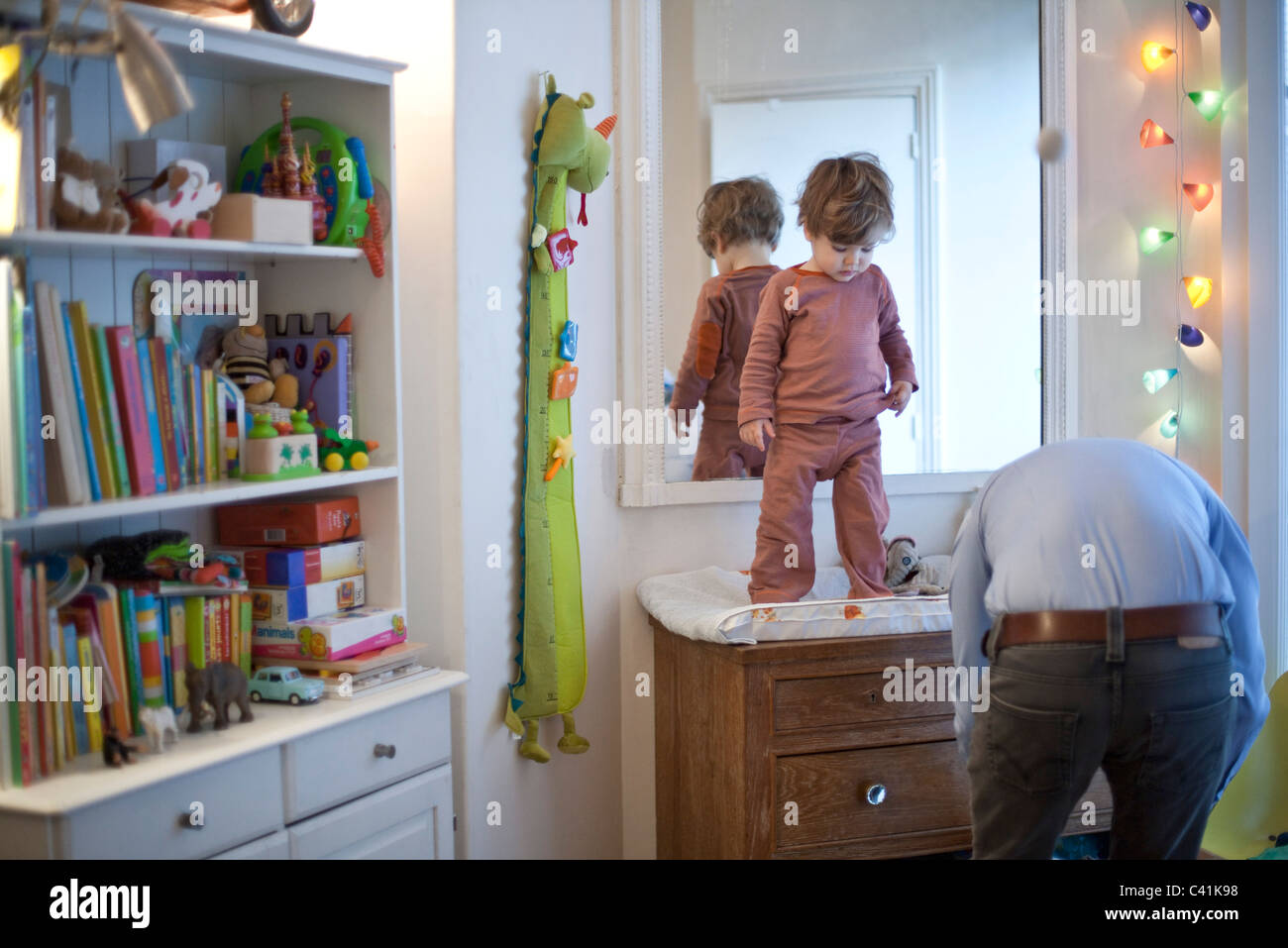 Toddler boy standing on top of changing table in nursery Stock Photo