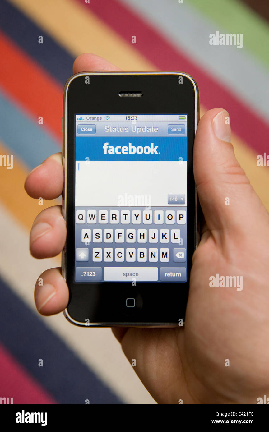 Close up of male hand holding an iPhone about to update his Facebook status. (Editorial use only). Stock Photo