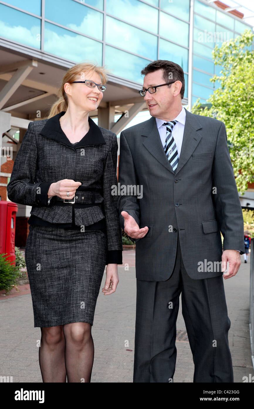 Man and woman wearing suits walking along talking. Stock Photo