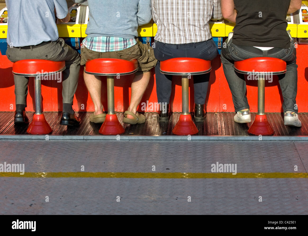 People sitting on stools in a fairground on Brighton Pier. Stock Photo