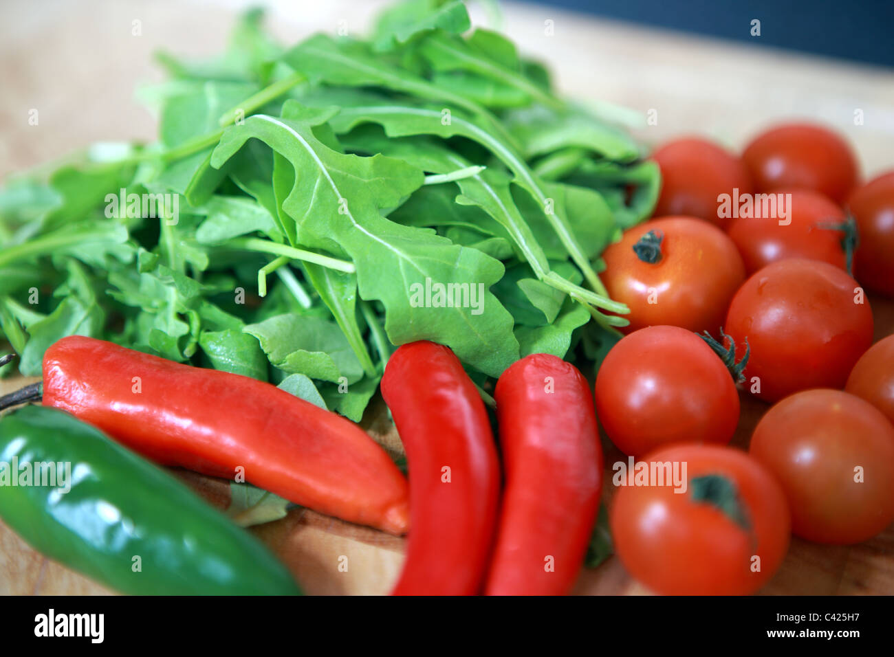 Rocket with cherry tomatoes, red and green peppers on a wooden chopping board Stock Photo