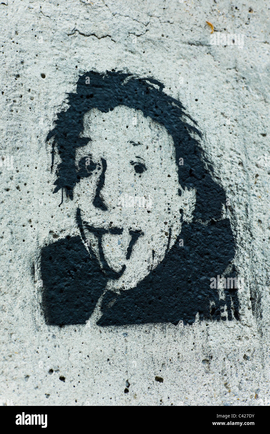 Stencil of the head of Albert Einstein sticking / poking out his tongue at the viewer on a gray concrete wall in Munich, Germany Stock Photo