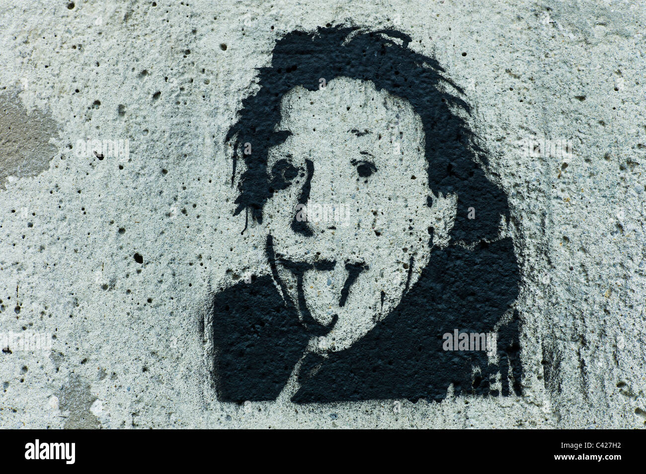 Stencil of the head of Albert Einstein sticking / poking out his tongue at the viewer on a gray concrete wall in Munich, Germany Stock Photo
