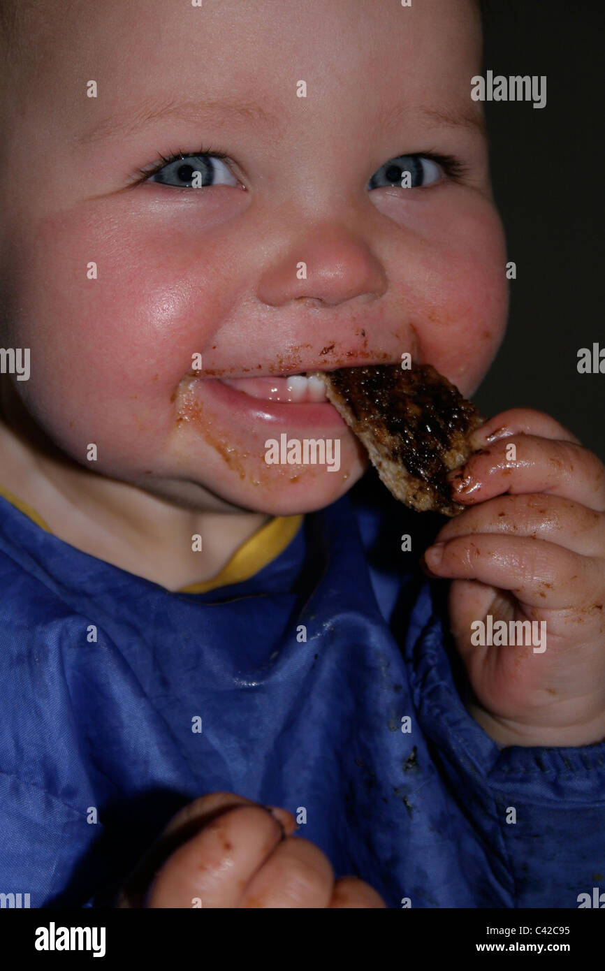 1 year old girl eating toast with marmite and getting it all over her face and hands Stock Photo