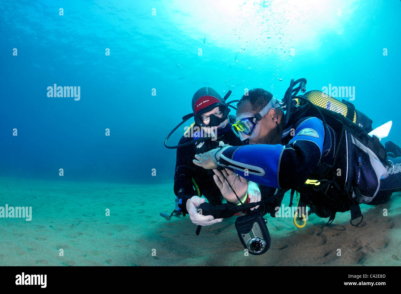 Two scuba divers, one giving signal of half used air other checking gauge Stock Photo