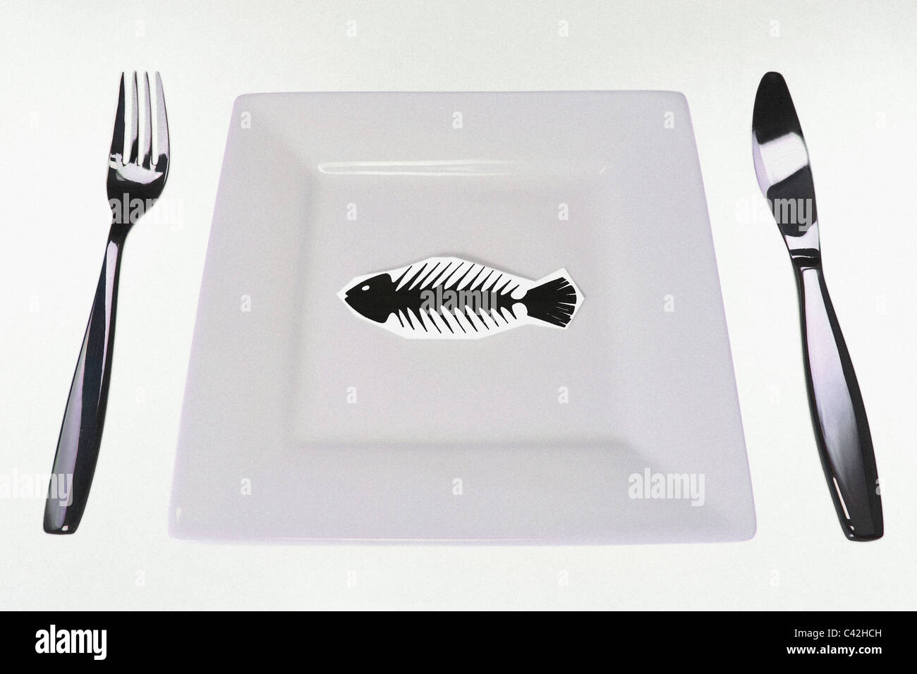 drawn fish skeleton in the middle of the dish and minimalistic kitchen set symbolizes poverty and starvation. Copy-space. Stock Photo