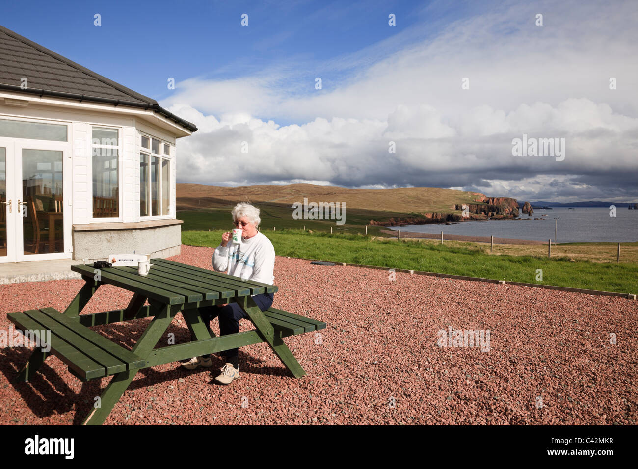 Female customer sat at a picnic table outside Braewick café in summer with a view along coastline. Eshaness Shetland Islands Scotland UK Stock Photo