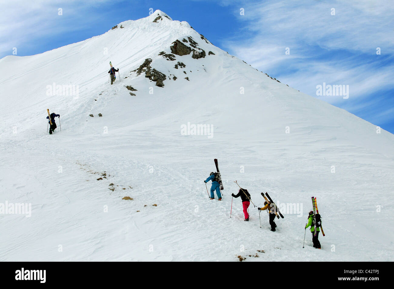 A group of skiers hike up a mountain ridge with his skis on their backs. Stock Photo