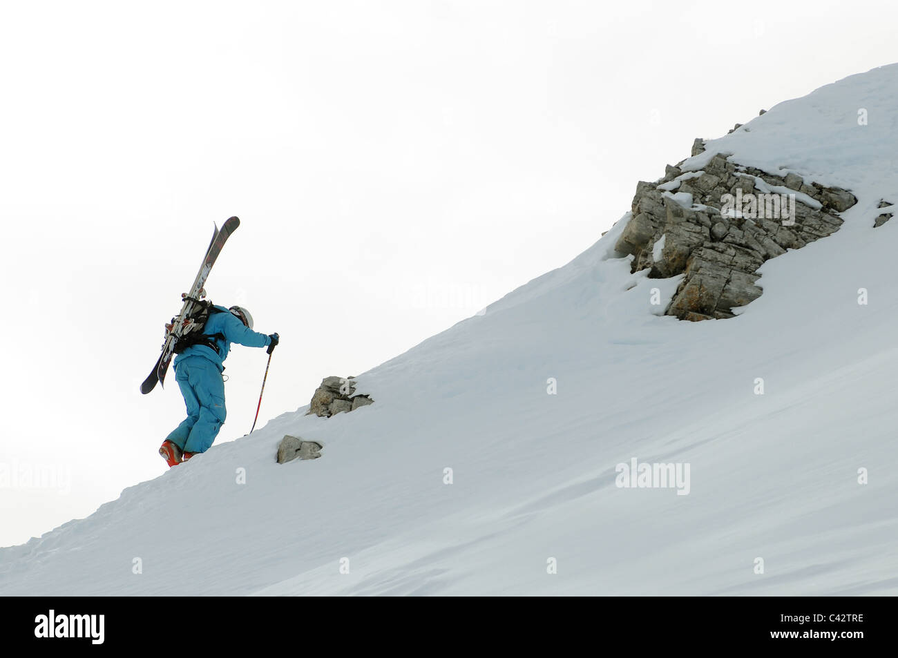 A skier hikes up a mountain ridge with his skis on his back. Stock Photo