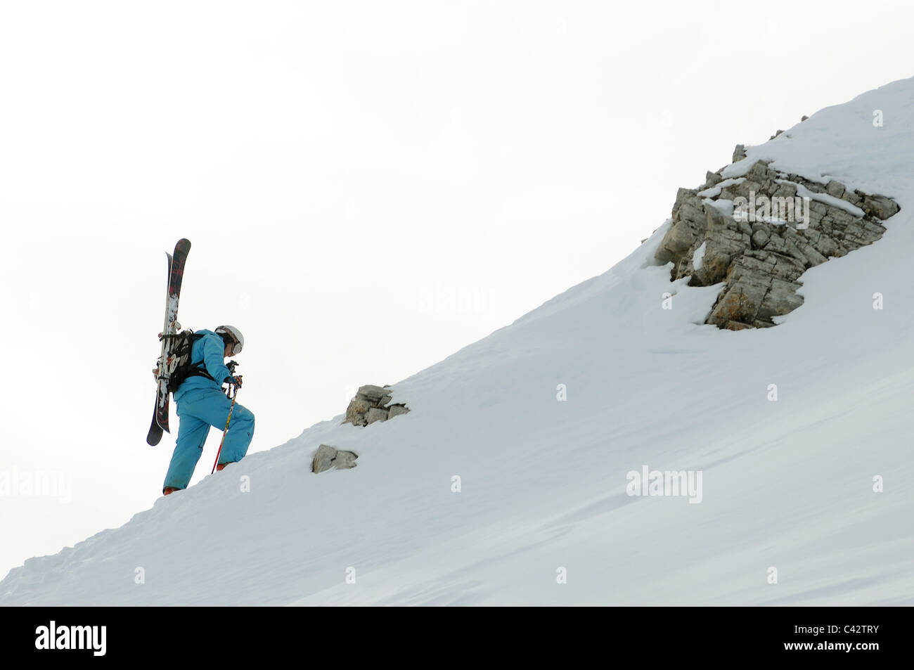 A skier hikes up a mountain ridge with his skis on his back. Stock Photo