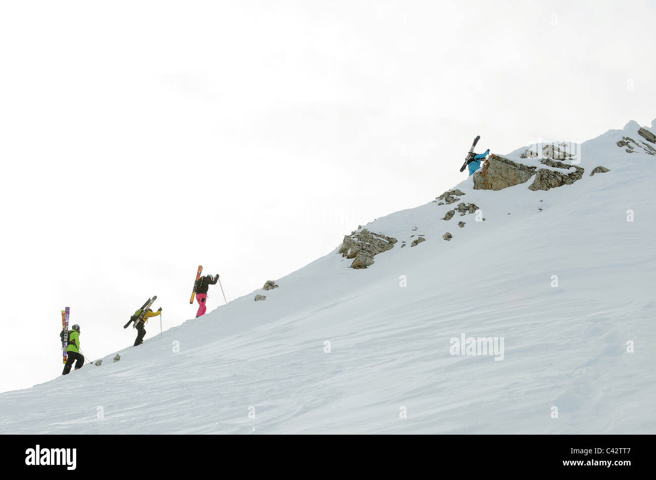 A group of skiers hike up a mountain ridge with his skis on their backs. Stock Photo
