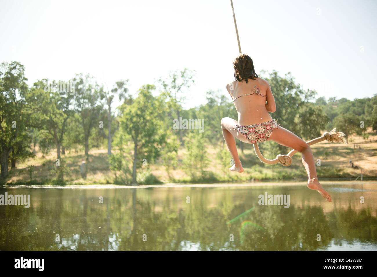 Girl Jumps Off A Rope Swing Into A Lake Stock Photo