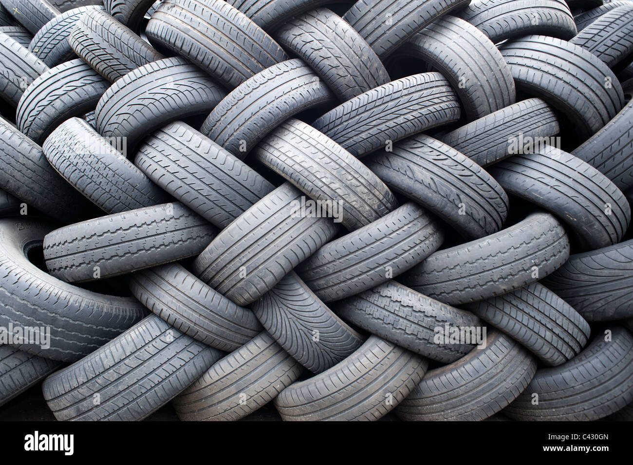 A large number of tyres sit neatly in an interwoven stacked pattern. Stock Photo